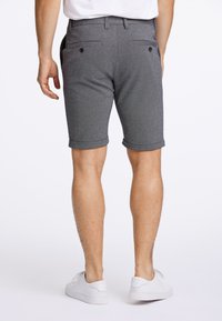 Graue Shorts mit glatter Textur, umgeschlagenen Säumen und zwei aufgesetzten Gesäßtaschen mit Knöpfen. Kombiniert mit weißen Turnschuhen.