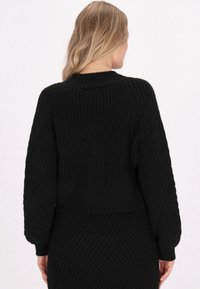 Schwarzer Strickpullover mit geripptem Textur, cropped Design, langen Ärmeln und rundem Halsausschnitt. Die Rückansicht betont die Nahtdetails.