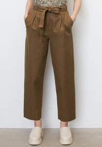 Pantalons marron taille haute avec un nœud papillon à l'avant, design plissé, poches latérales et longueur cropped. Associés à des sabots de couleur claire.