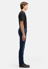 Czarny t-shirt z krótkim rękawem w połączeniu z granatowymi jeansami o dopasowanym kroju i czarnym obuwiem. Strój cechuje się prostym, dopasowanym fasonem.