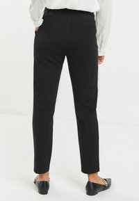 Zwarte op maat gemaakte broeken met een slim fit, voorzien van achterzakken en een zachte textuur. Gestyled met een ingestopt topje en zwarte flats.