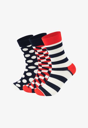 Trois paires de chaussettes en coton : bleu marine à pois blancs, rouge à motifs géométriques, et rayures bleu marine/blanc avec des accents rouges.
