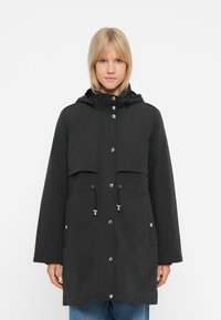 Giacca nera impermeabile con cappuccio, chiusura frontale a bottoni, vita regolabile con cordino e due grandi tasche applicate. Texture liscia e design casual.
