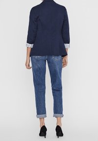 Marinblå kavaj med strukturerade axlar, grårandiga manschetter. Matchas med ljusblå jeans med uppvikt cuffs och svarta högklackade skor.