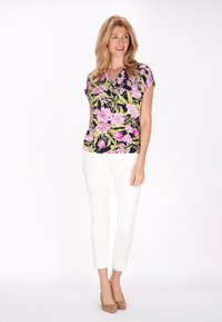Blomstret bluse med en marineblå baggrund, prydet med pink og grønne blomster. Knyttet sammen med tætsiddende hvide bukser og beige sko, hvilket skaber et afslappet look.