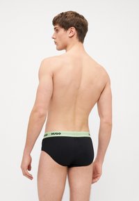 Culottes noires avec une taille légerement verte, arborant le logo "HUGO" en noir. Tissu lisse, design ajusté, style minimaliste.