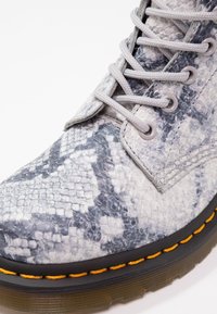 Gros plan sur une botte à motif peau de serpent gris et noir avec des lacets gris, une semelle noire et un détail de couture orange.