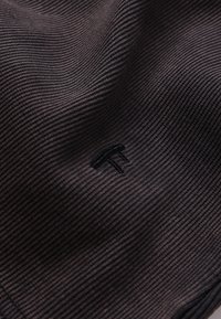 Μαύρο ριμπ ύφασμα με  απαλό υφή, διακοσμημένο διακριτικά με κεντημένο λογότυπο. Ο σχεδιασμός είναι απλός και λιτός, δίνοντας έμφαση στη λειτουργικότητα.