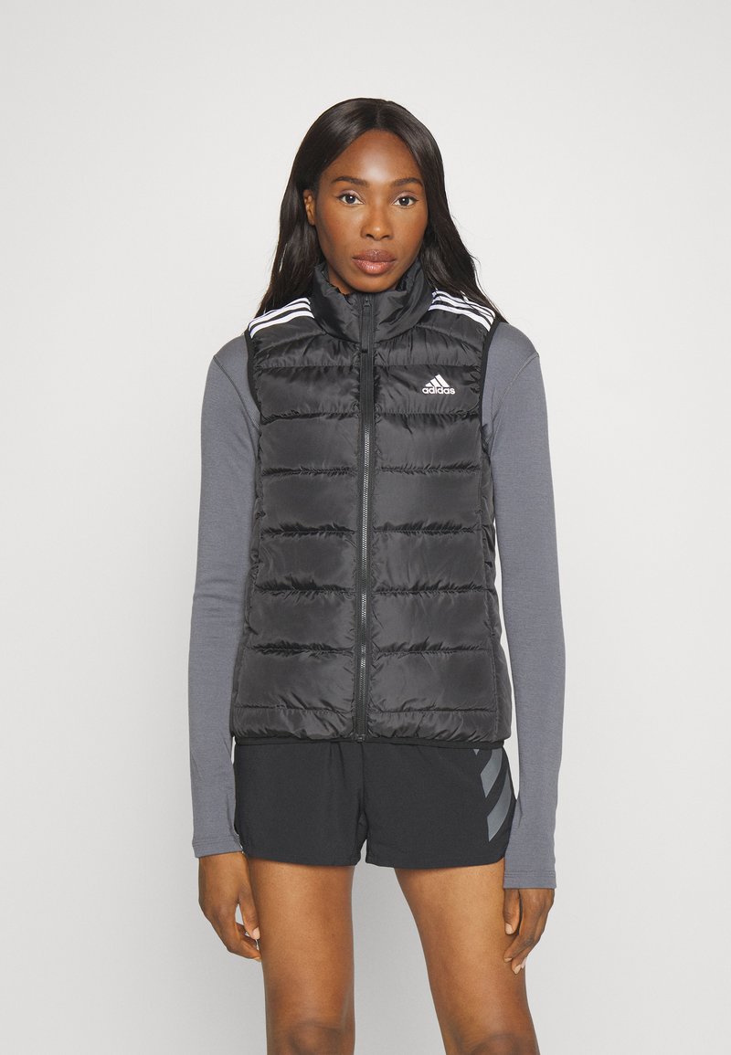 Fekete puffermellény, elülső cipzárral, vízszintes varrással, magas gallérral és fehér díszítéssel a vállakon. Könnyű és szigetelt.