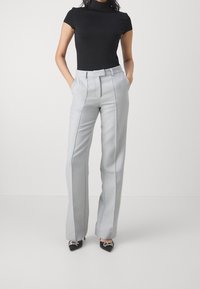 Šedé kalhoty na míru s vysokým pasem, bočními kapsami a rovným střihem nohavic. Kombinovány s černým přiléhavým rolákem a černými lodičkami na podpatku.