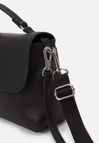 Czarna torebka ze skóry z teksturą, zamykana na klapę, wyposażona w srebrne okucia oraz odpinany materiałowy pasek o regulowanej długości.