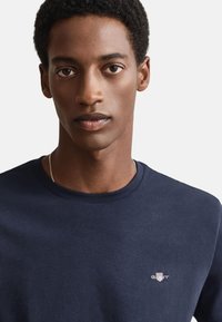 Mörkblå bomulls-T-shirt med rund hals och liten broderad logga på bröstet; mjuk textur med klassisk passform och korta ärmar.