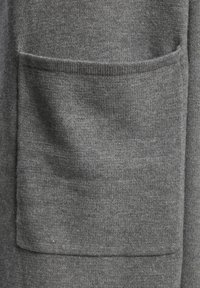 Pilkas megztinis su minkšta, tekstūrine medžiaga. Yra priekinė kišenė su rauktomis briaunomis, pabrėžiančiomis šilumą ir komfortą.