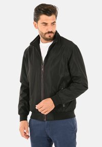 Giacca bomber nera con colletto alto, zip frontale, polsini ed elastico in vita. Presenta cuciture a contrasto e due tasche laterali.
