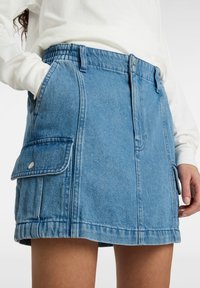 Denimhame vaaleansinisena, jossa on vauvan vyötärö, etutaskut läppäkiinnityksellä ja suora leikkaus keskireiteen pituudella.