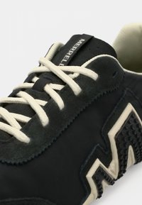 Μαύρο αθλητικό παπούτσι με επάνω μέρος από σουέτ και υφασμάτινο υλικό, εκρού κορδόνια, υφή από καουτσούκ και ξεχωριστό σχέδιο ζιγκ ζαγκ στη σόλα.