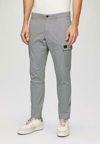 Grijze cargobroek met zijzakken, slim fit, gemaakt van lichtgewicht stof, met een knoopsluiting en stikseldetail. Draagt met witte sneakers.