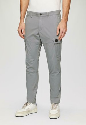 Grijze cargobroek met zijzakken, slim fit, gemaakt van lichtgewicht stof, met een knoopsluiting en stikseldetail. Draagt met witte sneakers.