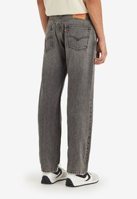Jeans de denim gris con corte recto, con un parche en la cintura y en los bolsillos traseros. Combinados con zapatillas blancas y una camisa crema.