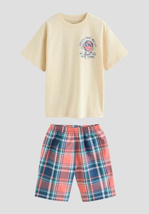 Karge kollane T-särk graafilise trükiga, kombinatsioonis rohekate lühikeste pantidega roosa, sinise ja valgega. T-särk omab ümarat kaelaauku ja lühikesi varrukaid.