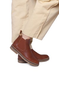 Botas de cuero marrón hasta el tobillo con inserciones elásticas en los laterales, punta redonda y costuras en contraste. Superficie texturada y lengüeta en el talón.