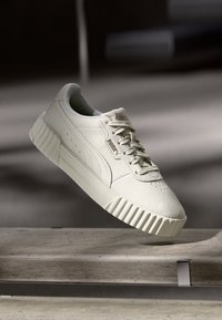 Witte sneaker met een structuur van suède bovenwerk, een rubberen zool met groeven en veters, met subtiele perforaties en merkdetails.