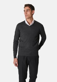 Maglione grigio scuro a collo a V realizzato in tessuto a maglia, caratterizzato da maniche lunghe e polsini a coste, abbinato a pantaloni neri e una camicia bianca sotto.