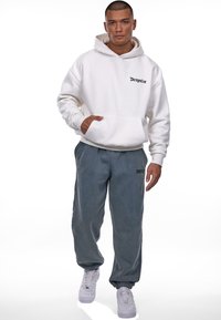 Hvid hoodie med frontlomme og sort "Dropsize" logo, parret med grå sweatpants og hvide sneakers med struktureret overflade og elastiske manchetter.