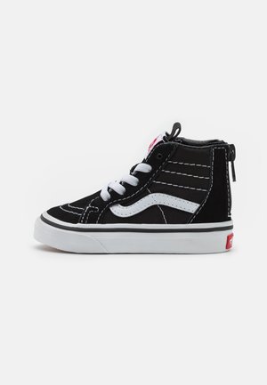 Black and white high-top sneakers with textured canvas, white stitching, a rubber sole, and a red logo tag on the heel.