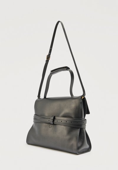 Sac à main en cuir noir avec poignée supérieure, bandoulière réglable et ceinture décorative autour du milieu, sur un fond uni.