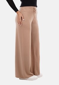 Pantaloni beige a gamba larga realizzati in tessuto morbido con vita regolabile; abbinati a sneaker bianche, che mostrano una trama liscia e una vestibilità rilassata.