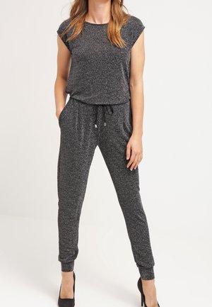 Jednoczęściowy kombinezon w jodełkę w czarno-białym kolorze, z krótkimi rękawami, elastyczną talią i zwężanymi mankietami, zestawiony z czarnymi szpilkami.