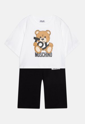 Maglietta bianca a maniche corte con grafica di un orso dei cartoni animati e testo "Toy Moschino", abbinata a pantaloni corti neri con il logo bianco "Moschino".