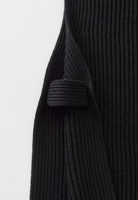 Pull noir en maille côtelée plié avec une manche partiellement remontée sur fond blanc.