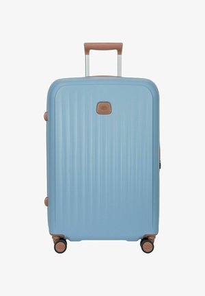Valigia rigida azzurro chiaro con maniglie marroni, quattro ruote girevoli e manico telescopico retrattile.
