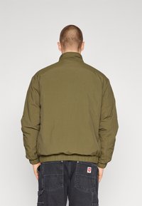 Giacca bomber imbottita verde oliva con colletto rialzato, polsini e vita elasticizzati. Design semplice, tessuto leggero e texture morbida.