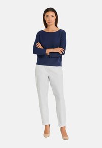 Marineblaues Strickpullover mit einem weiten Ausschnitt, kombiniert mit weißen, schmal zulaufenden Hosen und beigen High Heels, was einen ausgewogenen, neutralen Look schafft.
