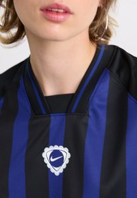Black and blue striped jersey with a V-neck design; features a white, scalloped Nike logo on the chest. Smooth fabric texture.