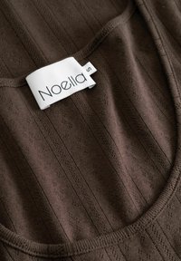 Rudos, briaunuoti marškiniai be rankovių, su mažais tekstūriniais akcentais, apvalia iškirpte ir balta etikete su užrašu "Noella S."