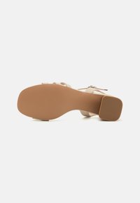 Sandale à talons beige avec une finition lisse, dotée d'une semelle galbée, de fines lanières et d'un talon carré texturé. Conçue pour le confort et le style.