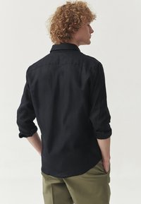 Zwarte linnen shirt met een kraag, lange mouwen opgerold tot aan de ellebogen en een rechte zoom. Eenvoudig ontwerp met minimale details op de achterkant.