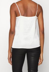 Camisón de satén blanco con finas tiras ajustables, textura suave, dobladillo recto y un diseño minimalista, combinado con pantalones negros ajustados.