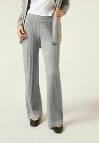 Pantalones acampanados de punto gris con textura de canalé, que cuentan con una cintura ancha y costuras sutiles. Combinados con un cárdigan gris claro y zapatos negros.