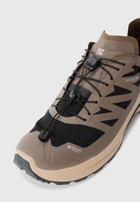 Brązowe i czarne buty sportowe GORE-TEX; syntetyczna cholewka z teksturowaną siateczką, bezpieczny system sznurowania oraz trwała gumowa podeszwa zapewniająca przyczepność.