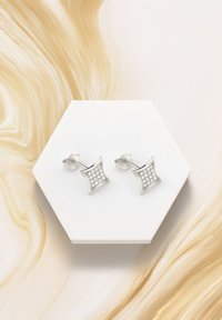 Silverfärgade studs med en fyrkantig, texturerad design som har ett rutnät av små klara ädelstenar, placerade på en vit hexagonal yta.