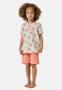 Ljust beige T-shirt med bruna prickar och en korallfärgad "SMILE"-tryck, matchat med korallfärgade shorts. Mjukt tyg, avslappnad passform, inga mönster på shortsen.