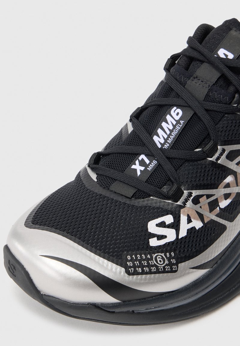Black athletic shoe featuring a mesh upper, silver accents, and a textured sole. Includes logo and model details on the side.