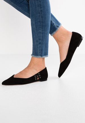 Czarne baleriny zamszowe z szpiczastym noskiem, ozdobione wycięciem i sznurowaniem po boku. Noszone z podwiniętymi niebieskimi dżinsami.