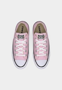 Ζευγάρι ροζ παπούτσια Converse All Star χαμηλού κόστους με λευκά κορδόνια και λαστιχένιες μύτες, εμφανιζόμενα από πάνω σε λευκό φόντο.