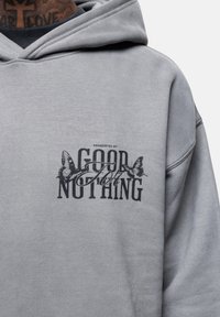 Felpa grigia con vestibilità comoda. Presenta un logo stampato in testo nero e grafiche di farfalle sul petto. Tessuto morbido e testurizzato.